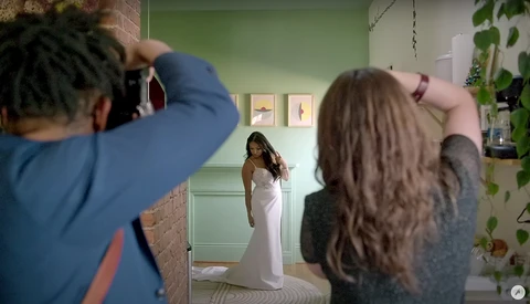 Photographer shooting a portrait of a woman in a white dress in a green studio room.