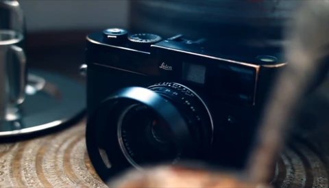 Black Leica rangefinder camera with lens in sharp focus on textured surface.