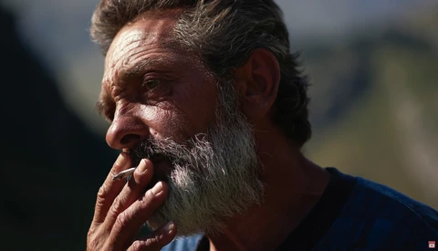 Bearded man in profile with hand near mouth, backlit by soft natural light.