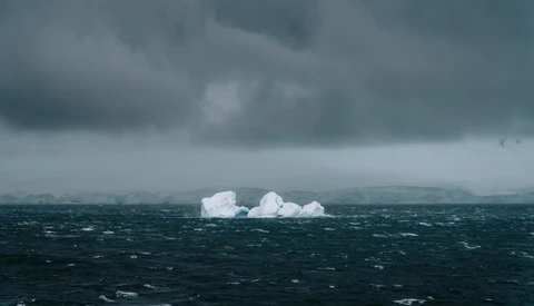 Icebergs floating in dark, choppy ocean waters beneath stormy gray clouds.