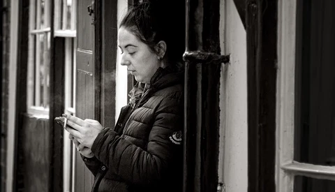 Woman in black quilted jacket checking her phone while standing in a doorway.