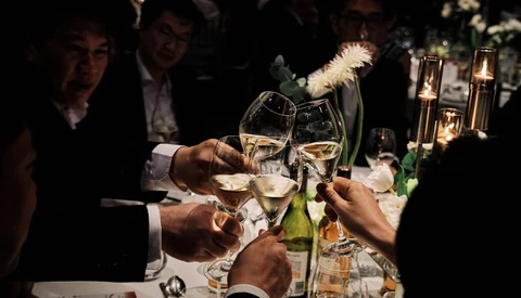 Multiple hands toasting with champagne glasses at an evening celebration.