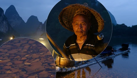 Fisherman wearing straw hat illuminated inside a circular reflector at dusk on a misty river with karst mountains.