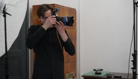 Photographer holding a DSLR camera with telephoto lens in a studio setting with professional lighting equipment.