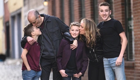 Five people of varying ages posing together on a brick-lined street, smiling at the camera.