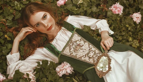 Woman in green dirndl dress reclining among pink roses and foliage.