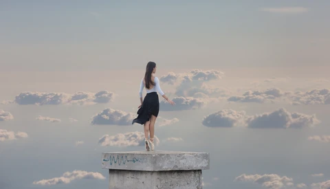 Woman standing on concrete pillar against dramatic cloudy sky.