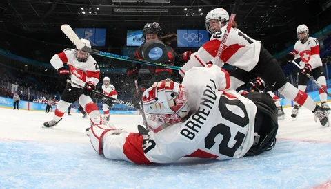 Hockey goalie in red and white uniform sprawled on ice after a save attempt during competitive match.