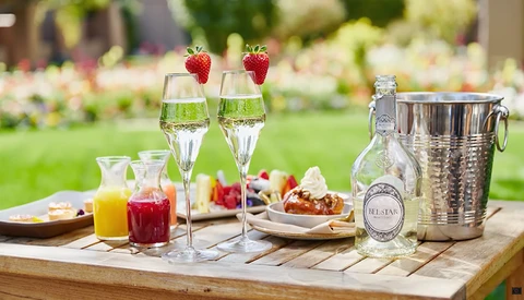 Outdoor garden table set with champagne flutes, strawberries, juice glasses, and a bottle in an ice bucket.