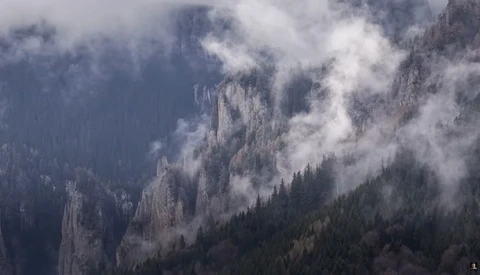 Misty mountain valley with forested slopes and dramatic cloud formations rolling through peaks.