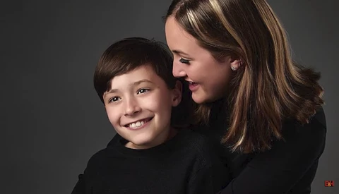 Woman and young boy smiling together against a gray background.