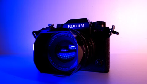 Fujifilm mirrorless camera with illuminated lens against blue and pink gradient background.