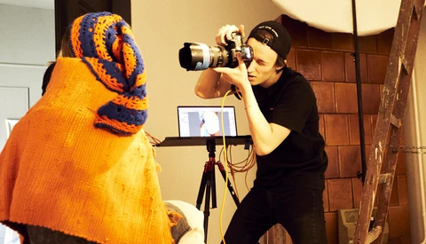 Photographer shooting a portrait of a person wearing an orange and blue knit sweater and headwrap.