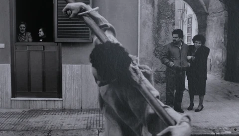 Black and white film still showing a figure suspended mid-air in an urban alleyway while pedestrians observe from nearby.