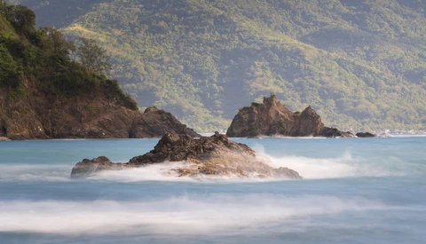 Rocky island formations surrounded by misty turquoise water with forested mountains in the background.