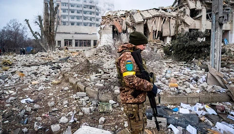 Soldier in camouflage walking through rubble of destroyed residential buildings.