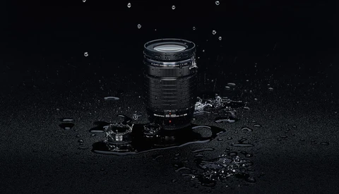Telephoto lens surrounded by water droplets and debris on dark wet surface.