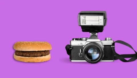 A hamburger and a vintage rangefinder camera with flash unit side by side on a magenta background.