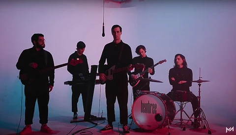 Five-piece band performing on stage with purple and blue gradient lighting.