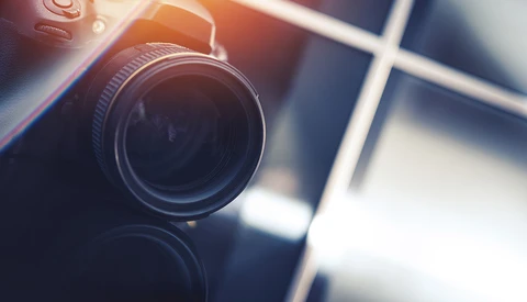 Close-up of a camera lens with warm golden sunlight and window shadows in the background.