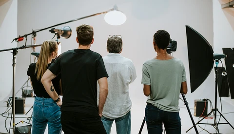 Four people viewed from behind in a professional studio with lighting equipment and softboxes.