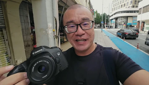 Photographer holding Canon EOS camera with standard lens on an urban street.