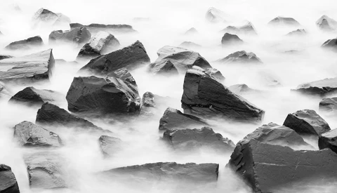 Rocks partially submerged in flowing water with long exposure effect creating smooth, misty texture.