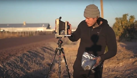Photographer with vintage camera on tripod in open field during golden hour.