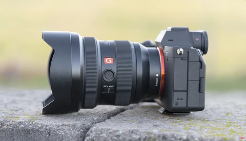Sony mirrorless camera with ultra-wide zoom lens and lens hood mounted on concrete surface.