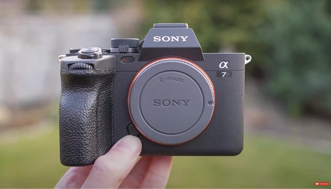 Sony α7 mirrorless camera body held in hand against blurred outdoor background.