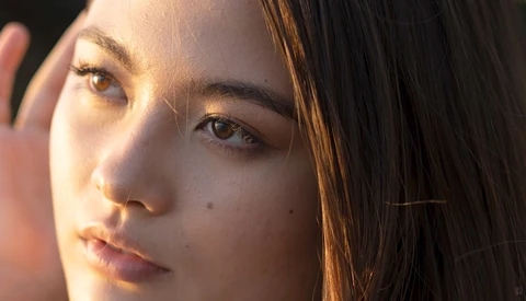 Woman's face in golden hour sunlight, looking directly at camera with natural expression.