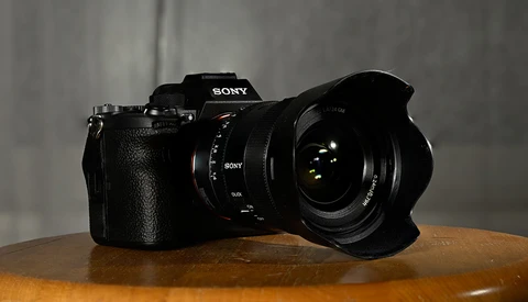 Sony mirrorless camera with wide-angle lens mounted, positioned on wooden surface against gray backdrop.