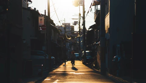 Cyclist riding alone down a narrow urban alley at golden hour with strong backlit sun creating dramatic shadows.