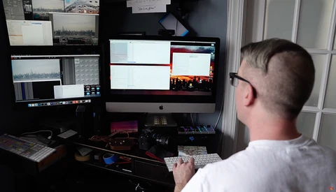 Photographer working at a dual-monitor editing workstation with color-graded footage displayed.