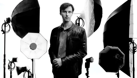 Man in leather jacket posed among professional studio lighting equipment and softboxes.