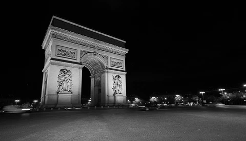 Illuminated neoclassical triumphal arch at night with detailed sculptural reliefs and ornamental panels.