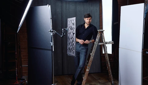 Photographer standing on a wooden ladder in a studio setup with professional lighting equipment and reflectors.