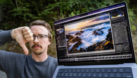 Photographer giving thumbs down gesture while laptop displays coastal landscape photo in editing software.