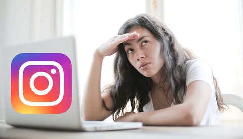 Woman at desk with hand to forehead looking at laptop displaying Instagram logo.