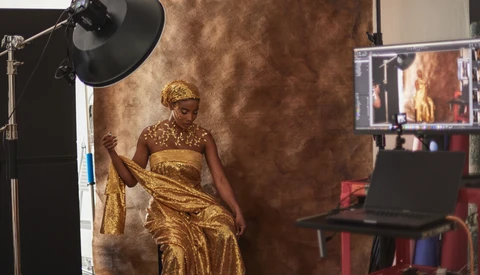 Woman in gold dress and headwrap posing on set with professional studio lighting and textured backdrop.