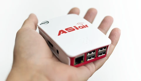Hand holding a small white and red Astian networking device with USB ports and ethernet connection.