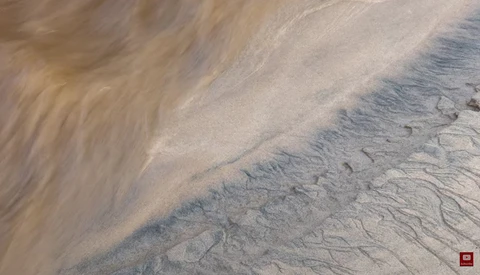 Aerial view of rippled sand patterns and water-carved channels on a desert or beach surface.