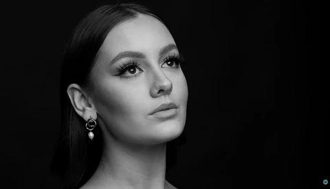 Woman in profile against black background with dramatic side lighting and defined eye makeup.