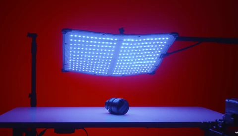 Blue LED panel light suspended above a table with a spherical object in moody red and blue studio lighting.