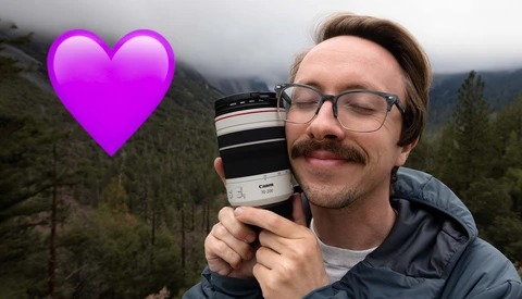 Photographer holding a Canon telephoto lens in a misty forested mountain landscape, with a bright magenta heart emoji overlay.