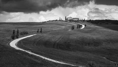 Winding white road cutting through rolling hills in black and white landscape photography.