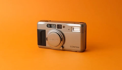 Contax compact camera with silver body and black accents on orange background.