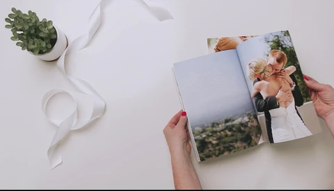 Hand holding open wedding photo album with couple image visible on pages.