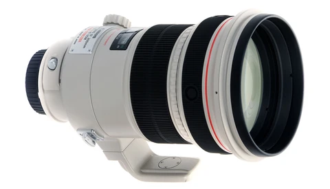 White telephoto lens with internal focus mechanism and red ring accent, shown in profile against white background.
