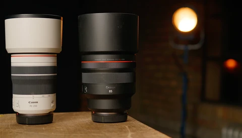Two telephoto lenses side by side on wooden surface with warm studio lighting in background.